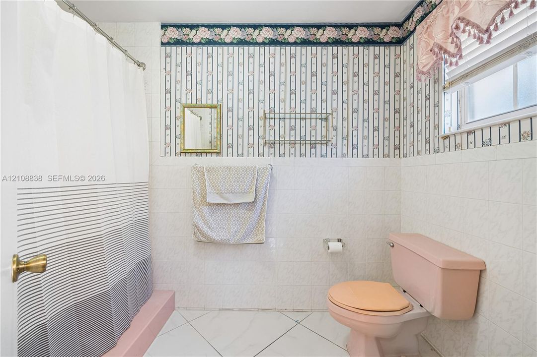 Bathroom featuring white tile wall cladding, patterned wallpaper, a built-in wall-mounted glass shelf, and a shower area with a raised platform