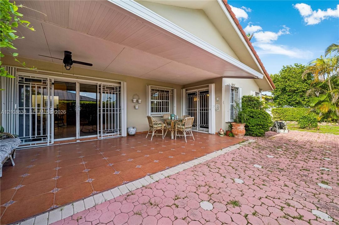 Covered patio featuring terracotta-style tile flooring, ceiling fan, and sliding glass doors with security screens, opening onto a concrete paver hardscape