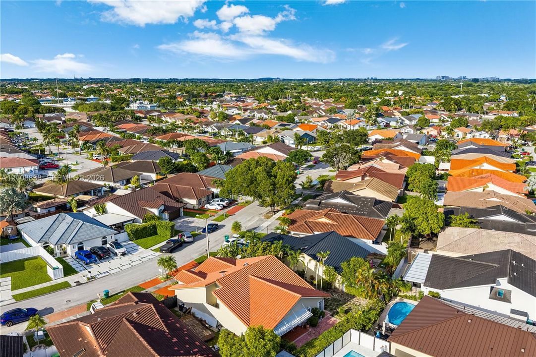 Aerial perspective of a residential neighborhood featuring paved streets, mature trees, multi-pitched rooflines, and private swimming pools