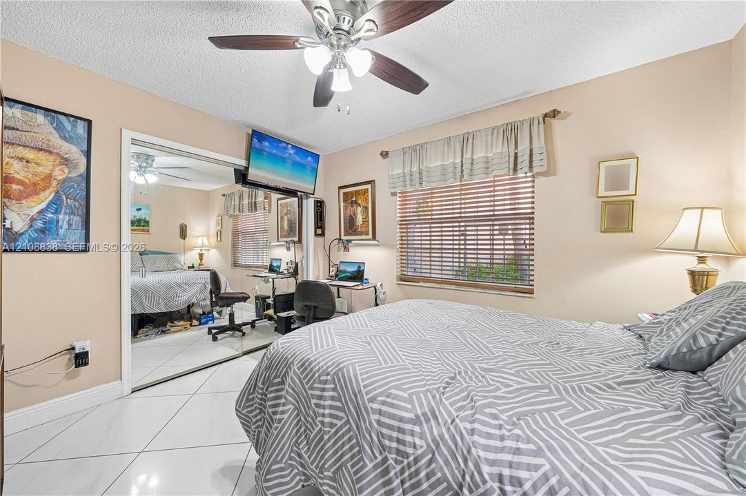 Room featuring large-format ceramic tile flooring, a mirrored sliding-door closet, a multi-blade ceiling fan with integrated light fixture, and horizontal window blinds