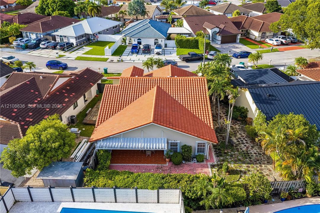 Aerial perspective featuring a terracotta-tiled roof, a covered patio with masonry flooring, and mature landscaping