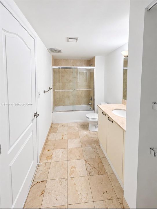 Full bathroom featuring stone tile flooring, a tub-shower combination with a glass sliding enclosure, stone wall surround, and a vanity with an integrated basin and stone countertop