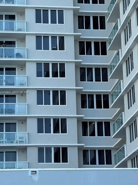 High-rise exterior featuring a light gray facade, multi-level balconies with glass railings, and expansive rectangular windows