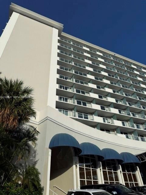 High-rise building exterior featuring tiered balconies with glass railings, structural columns, and arched blue awnings