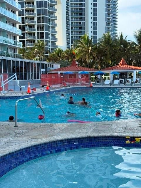 Outdoor swimming pool and spa featuring stone decking, blue tile trim, and multiple covered cabanas