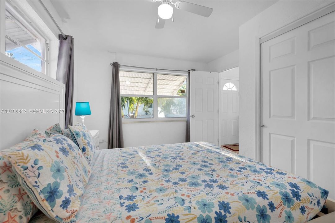 Neutral-toned bedroom featuring white walls, dual windows with natural light, a ceiling fan with light fixture, and a multi-panel closet door