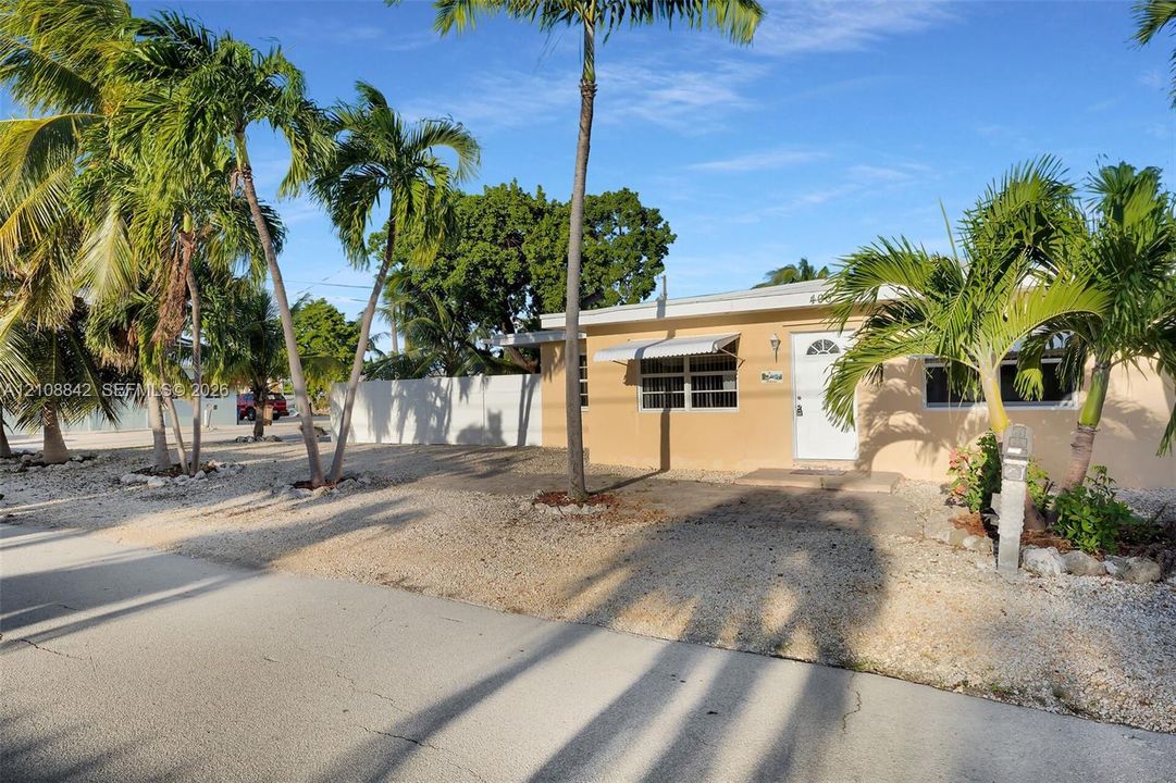 Single-story residence featuring light-toned exterior siding, metal window awnings, horizontal-sliding windows, and mature palm trees