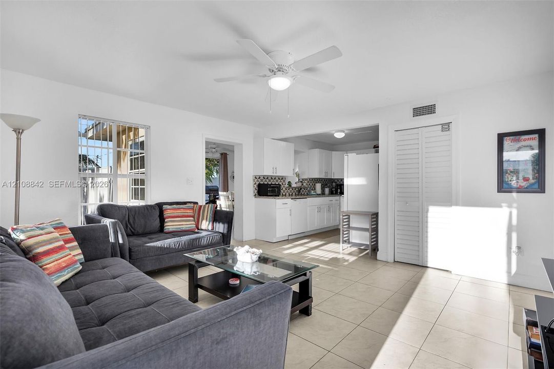 Open-concept interior featuring light-colored tile flooring, white cabinetry, a grid-patterned window, and a ceiling fan with integrated lighting