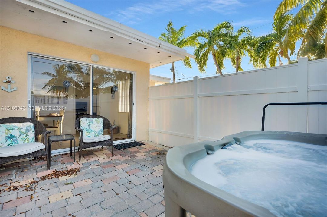 Private patio featuring stone paver flooring, a built-in hot tub, and a white vinyl privacy fence