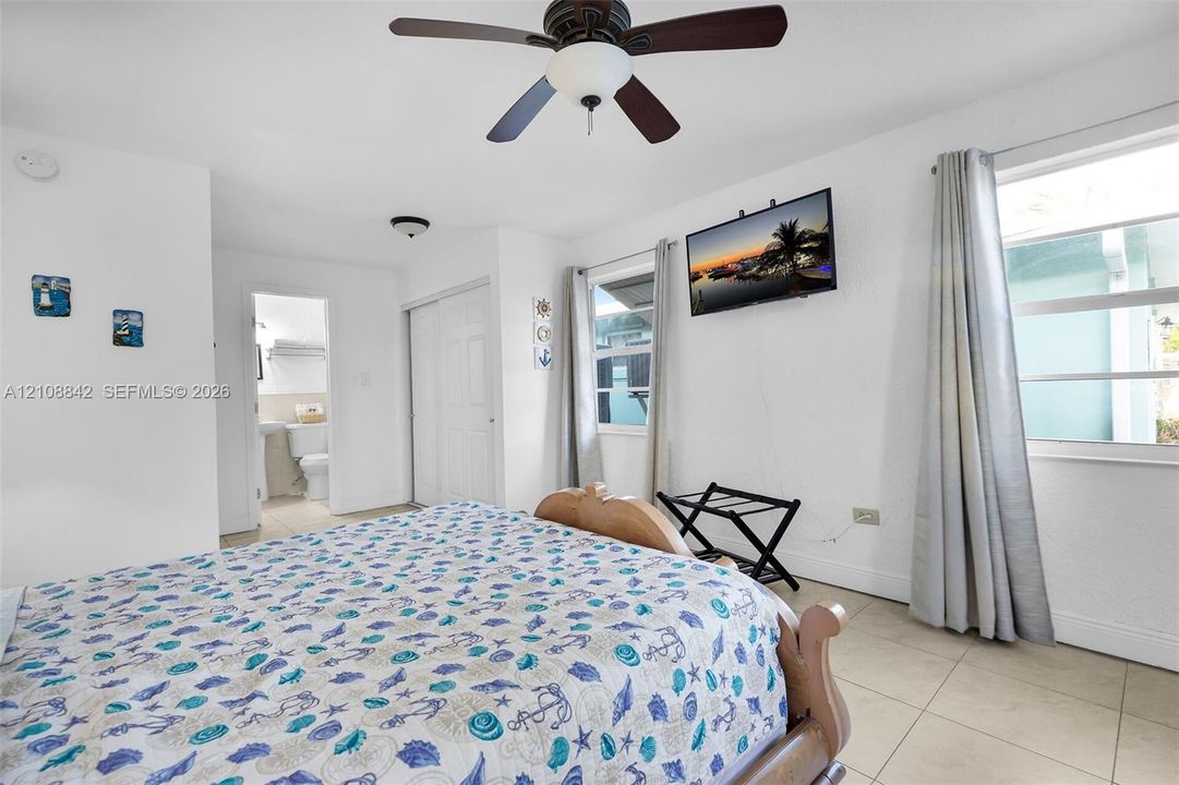 Bedroom featuring tile flooring, a ceiling fan with integrated lighting, dual windows with wall-mounted hardware, and a sliding-door closet