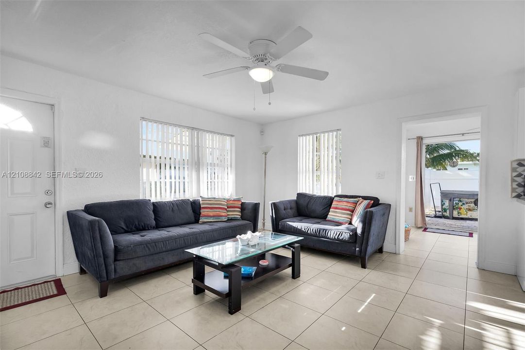 Living area featuring large format tile flooring, white-painted walls, and a ceiling fan with integrated lighting