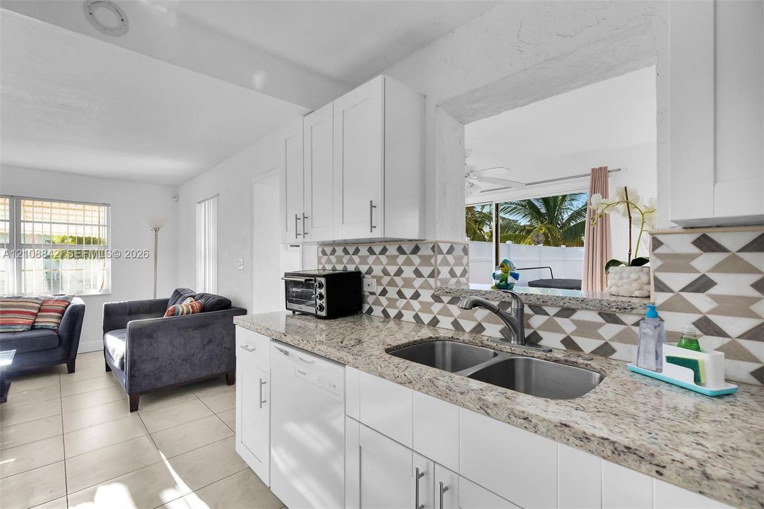 Kitchen featuring white shaker-style cabinetry, patterned tile backsplash, stone-finish countertops, and an undermount double-basin stainless steel sink with a pull-down faucet