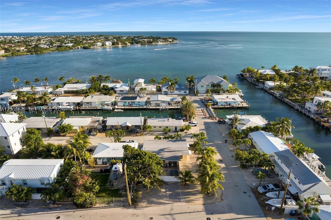 Aerial perspective of a coastal residential community featuring deep-water canal access, private boat docks, mature tropical landscaping, and immediate proximity to the open bay