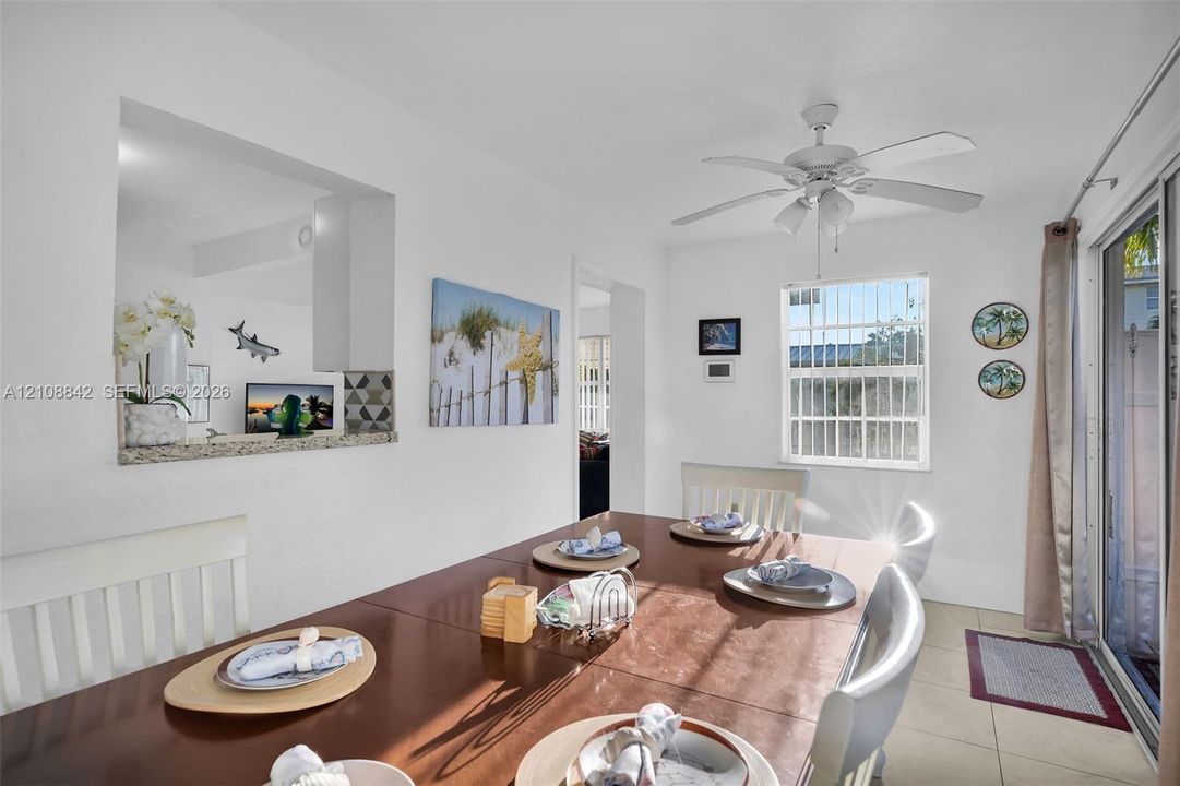 Dining area featuring tile flooring, a ceiling fan, sliding glass doors, and a kitchen pass-through window with a stone-finish countertop
