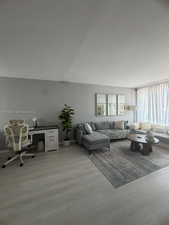 Open-concept interior featuring neutral wall paint, wood-finish flooring, and large-scale windows with floor-to-ceiling drapery