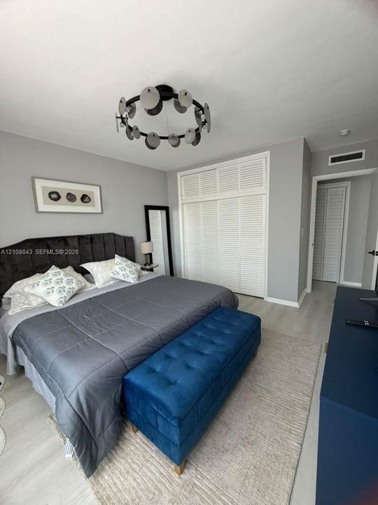 Neutral-toned interior featuring louvered closet doors, light wood-finish flooring, and a decorative circular multi-disk ceiling fixture
