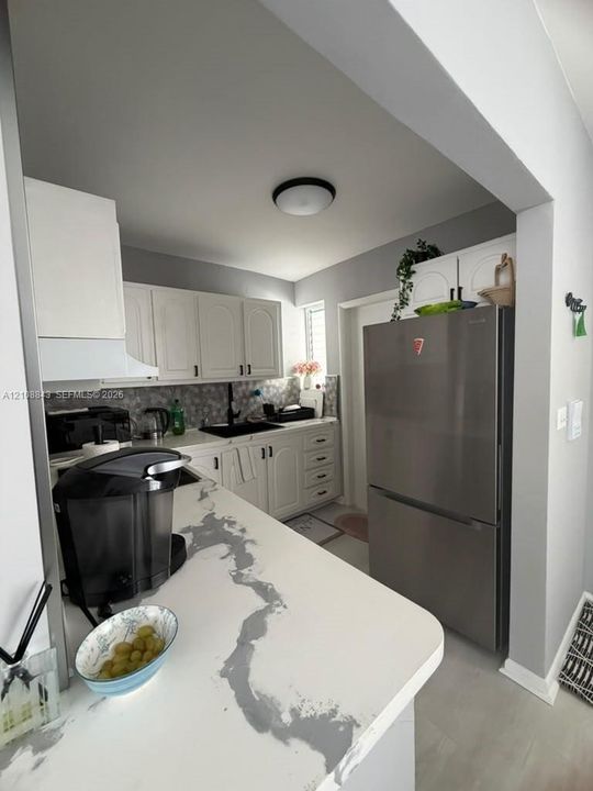 Kitchen featuring white cabinetry, stone-patterned countertops, a stainless steel refrigerator, patterned tile backsplash, and a black faucet