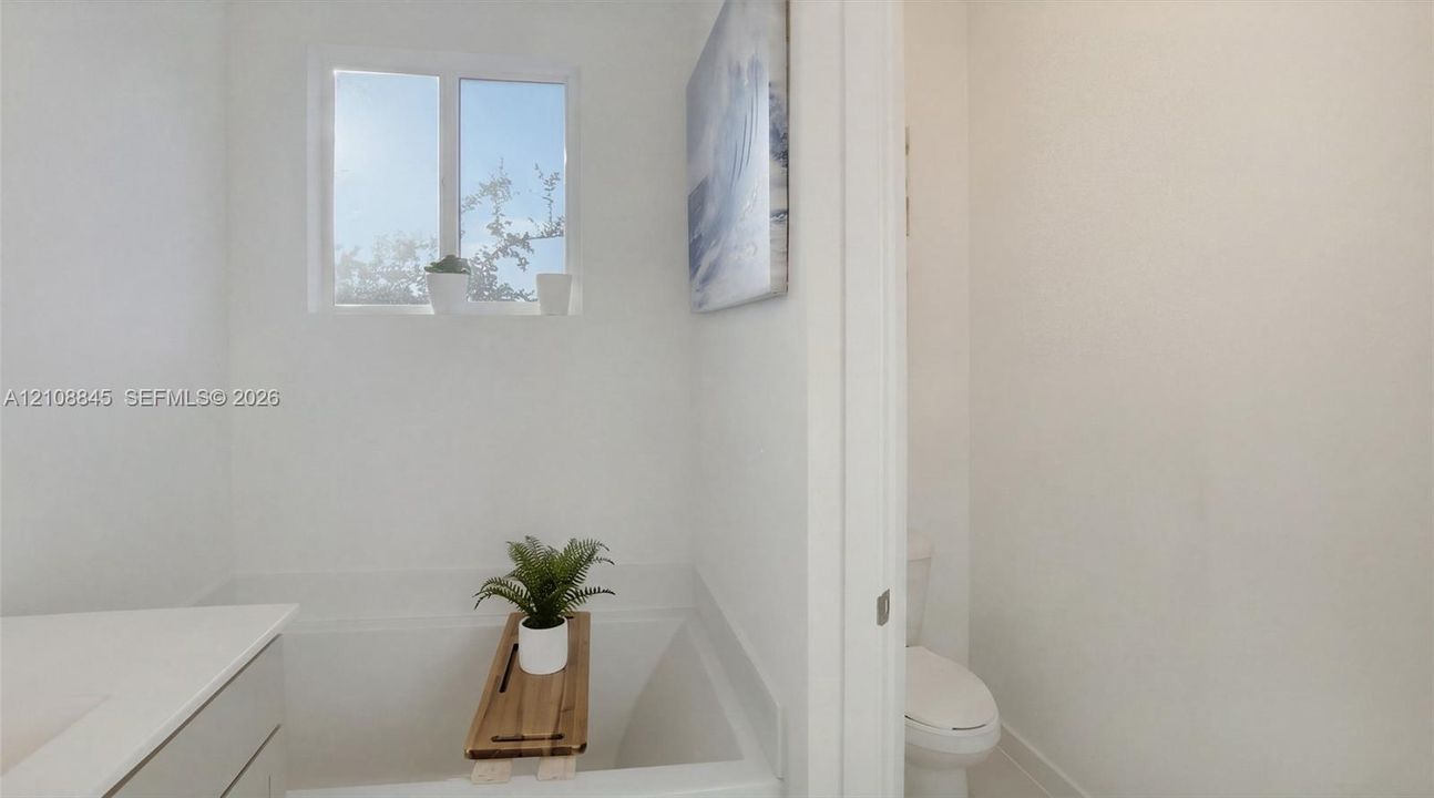 Full-width soaking tub, clean-lined white cabinetry, quartz countertop, and integrated plumbing fixtures