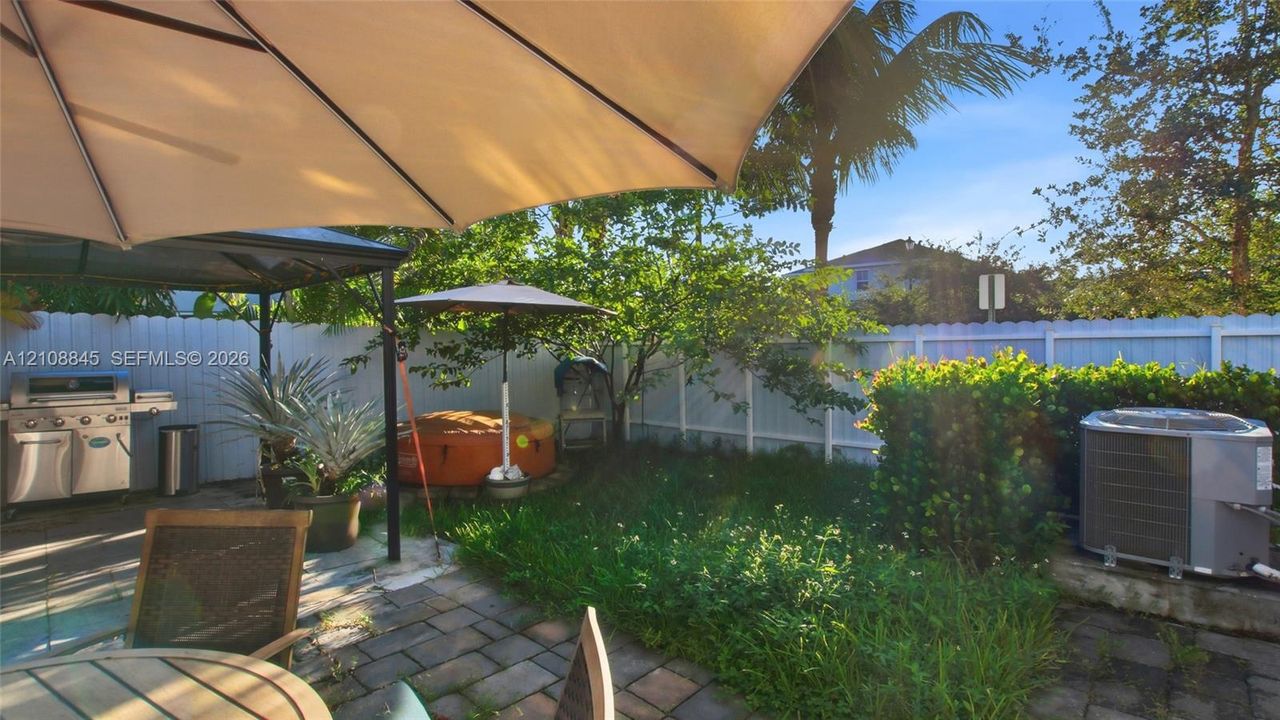 Fenced backyard featuring a paved stone patio, built-in stainless steel outdoor grill, and mature landscaping