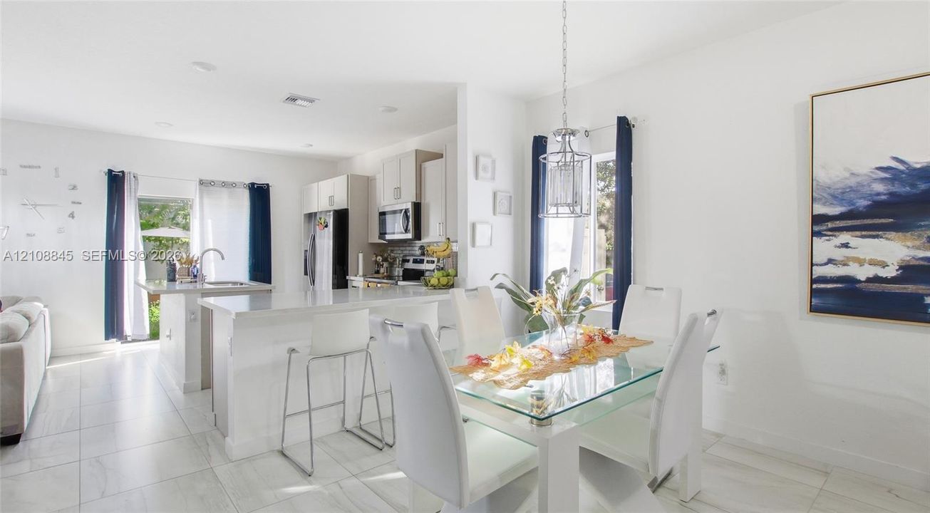 Open-concept interior featuring porcelain tile flooring, a custom-painted accent wall with decorative molding, a kitchen island with stone countertops, and a modern tiered chandelier