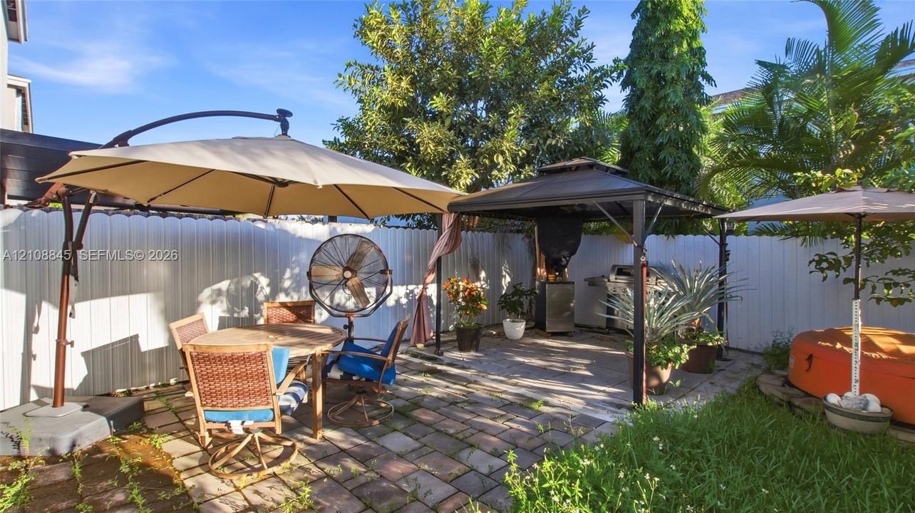Enclosed rear patio featuring paver stone flooring, a metal-framed gazebo, and perimeter vinyl fencing