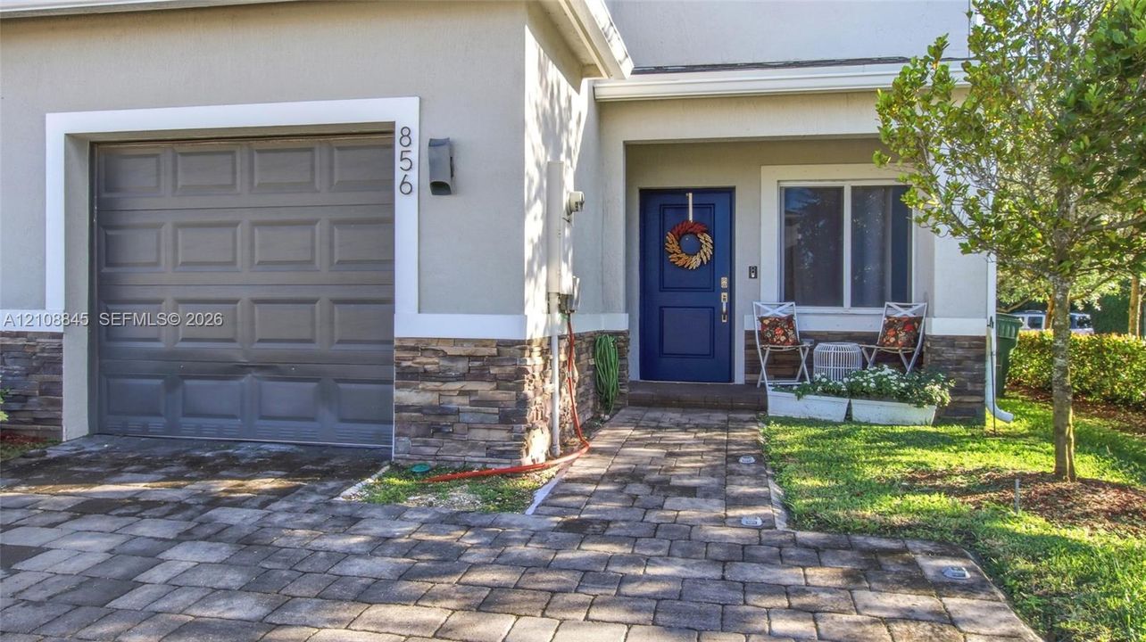 Stucco exterior facade featuring stone veneer masonry, paver walkway, single-car garage, and blue entry door