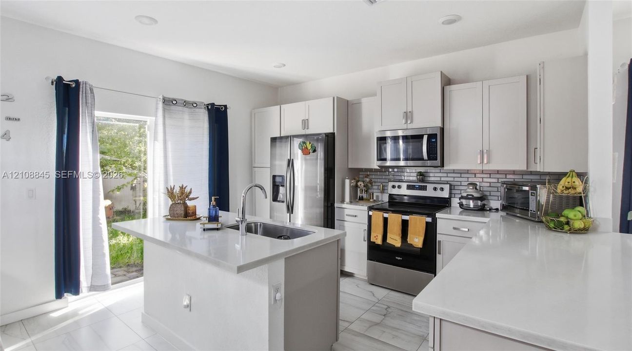 Kitchen featuring light-toned cabinetry, quartz countertops, subway tile backsplash, stainless steel appliances, and a central island with an integrated sink