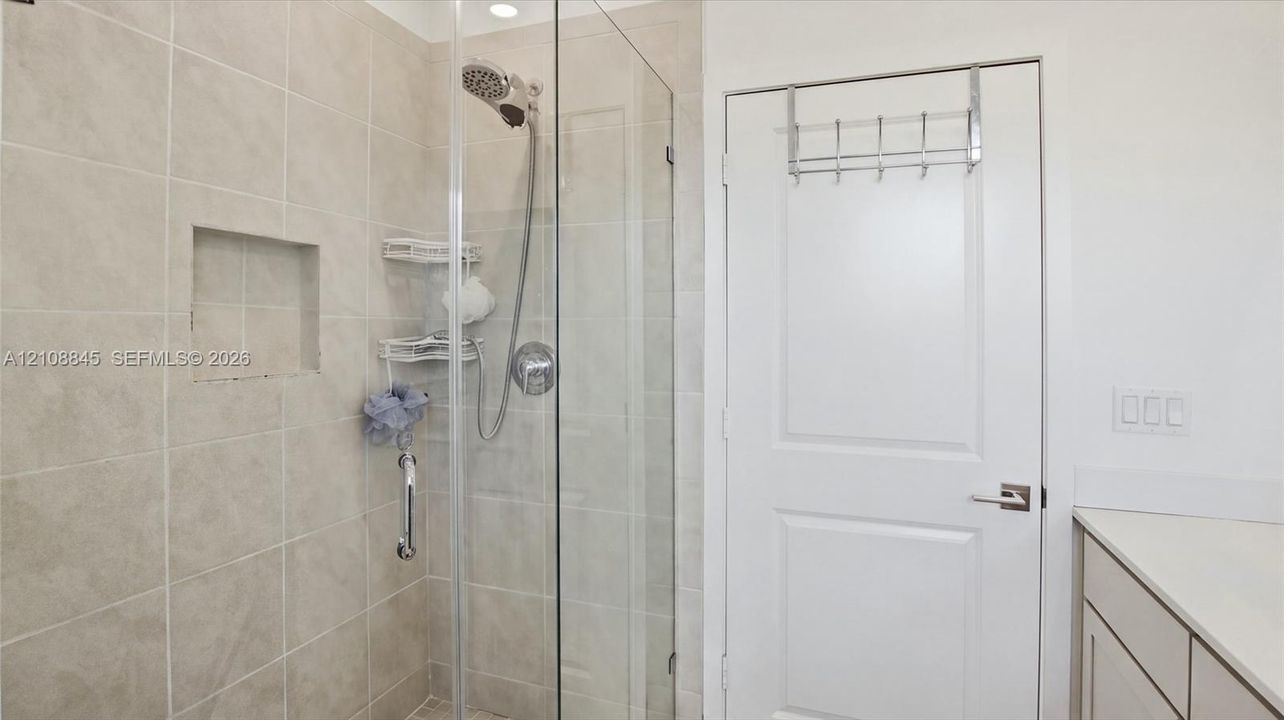 Walk-in shower featuring a frameless glass door, light-toned wall tile, a recessed niche, and a handheld showerhead fixture