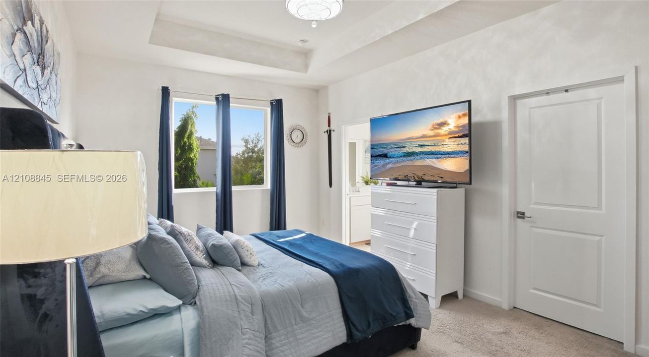 Bedroom featuring a tray ceiling, neutral wall coloring, carpeted flooring, and a multi-panel interior door