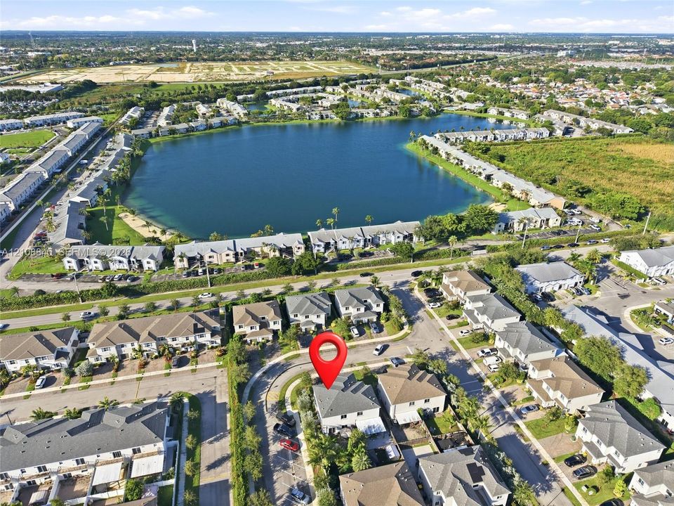 Aerial perspective of a multi-story residential structure featuring a gray shingle roof, asphalt-paved streets, and proximity to a large community lake