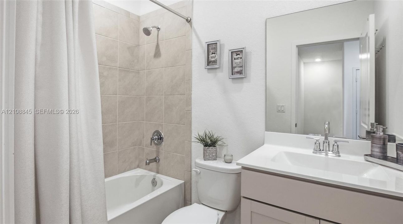 Bathroom featuring a vanity with an integrated sink and countertop, a large wall-mounted mirror, a tub-shower combination with tile surround, and chrome plumbing fixtures