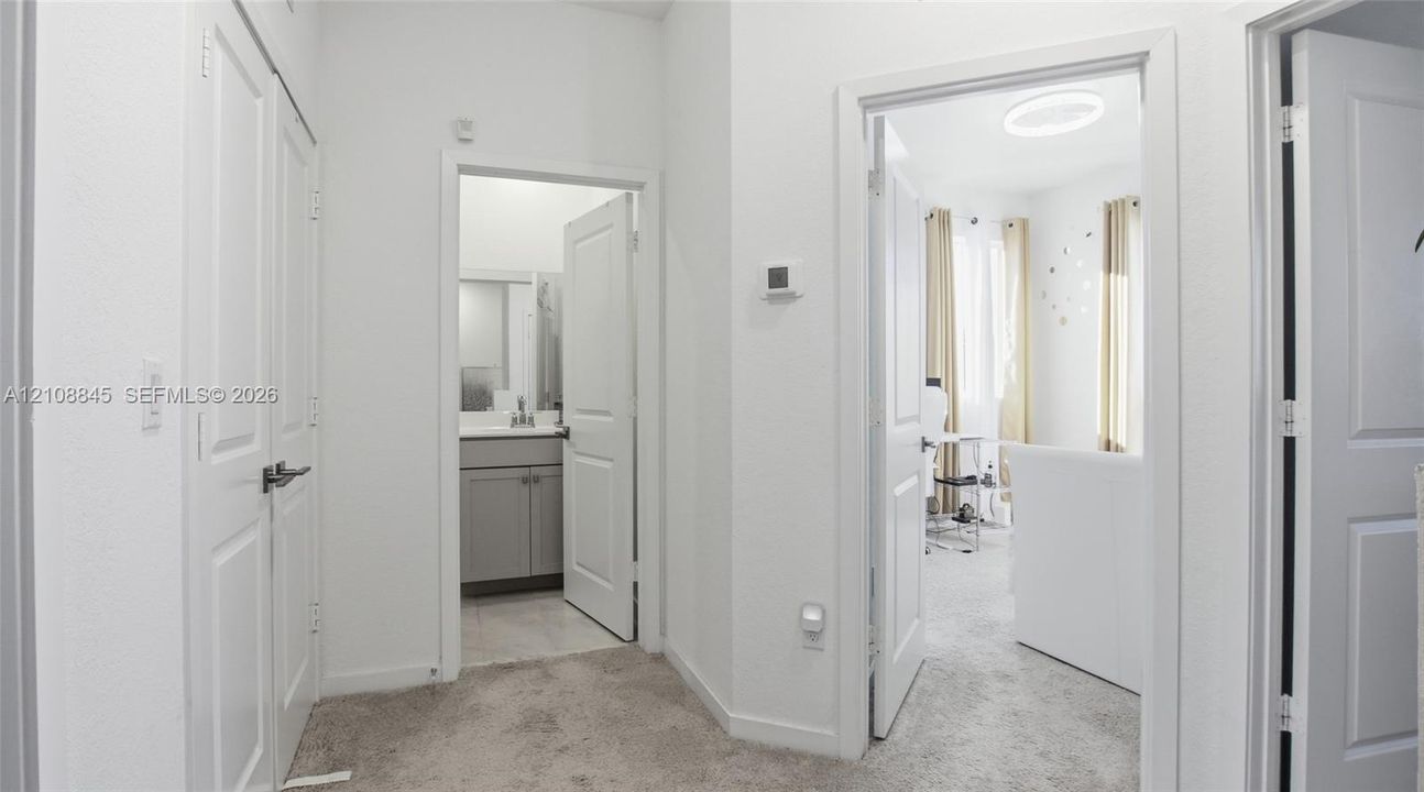 Interior hallway featuring multi-panel interior doors, neutral carpeting, and access to a bathroom with a grey vanity cabinet and stone-surfaced countertop