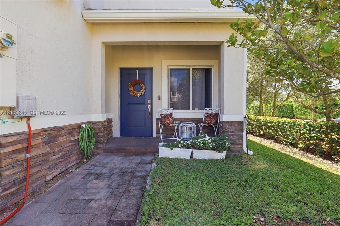 Covered entryway featuring a solid-color panel door, natural stone veneer siding, and a paver walkway