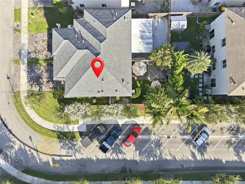 Aerial perspective of a multi-gabled shingle roof, corner lot placement, and exterior landscaping with mature trees