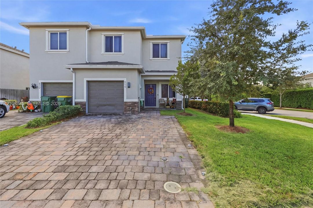 Two-story exterior featuring a paver driveway, stone facade accents, an integrated garage, and a covered entry