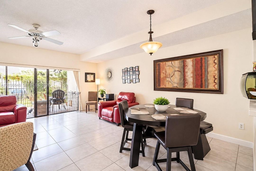 Open living area featuring neutral tile flooring, a ceiling fan with integrated lighting, a bowl-style pendant light fixture, and sliding glass doors