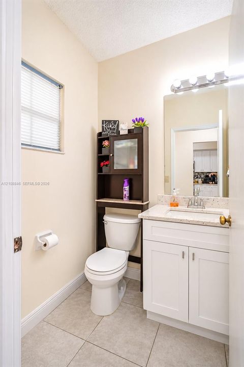 White vanity with stone-composite countertop, undermount sink, ceramic tile flooring, and integrated wall mirror with overhead light fixture