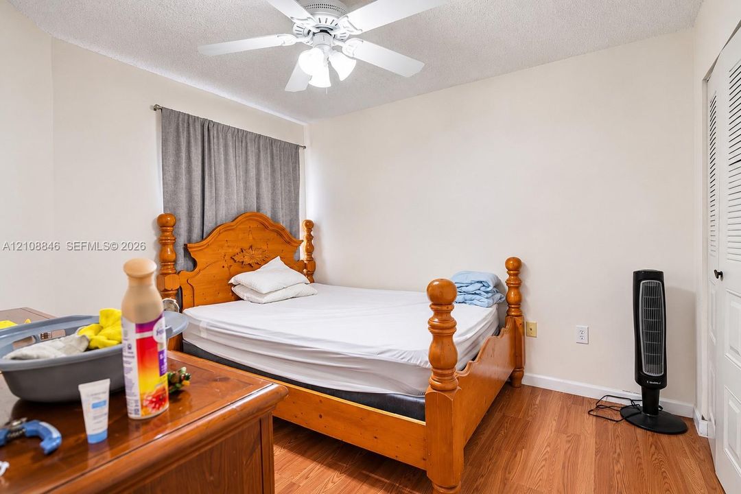 Bedroom interior featuring wood-finish flooring, white walls, a ceiling fan with integrated lighting, and louvered closet doors