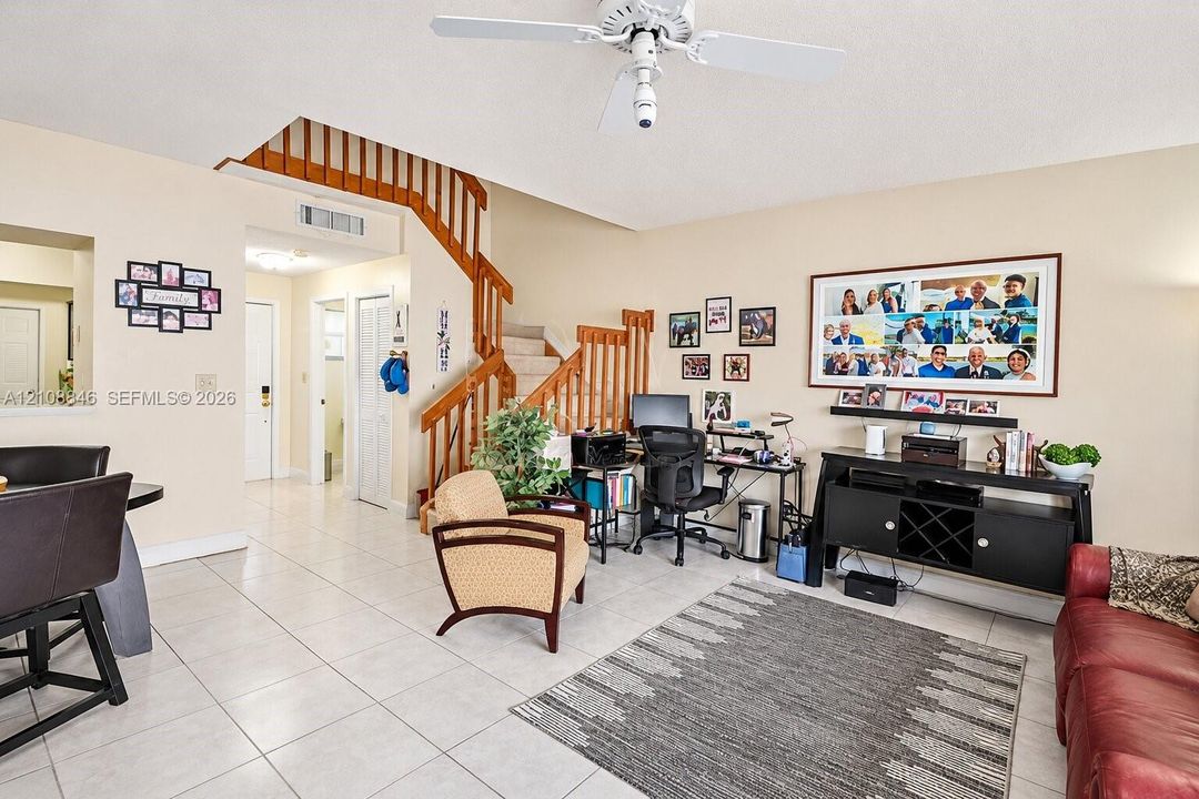 Open-concept interior featuring oversized tile flooring, a staircase with wooden railings, and a ceiling fan