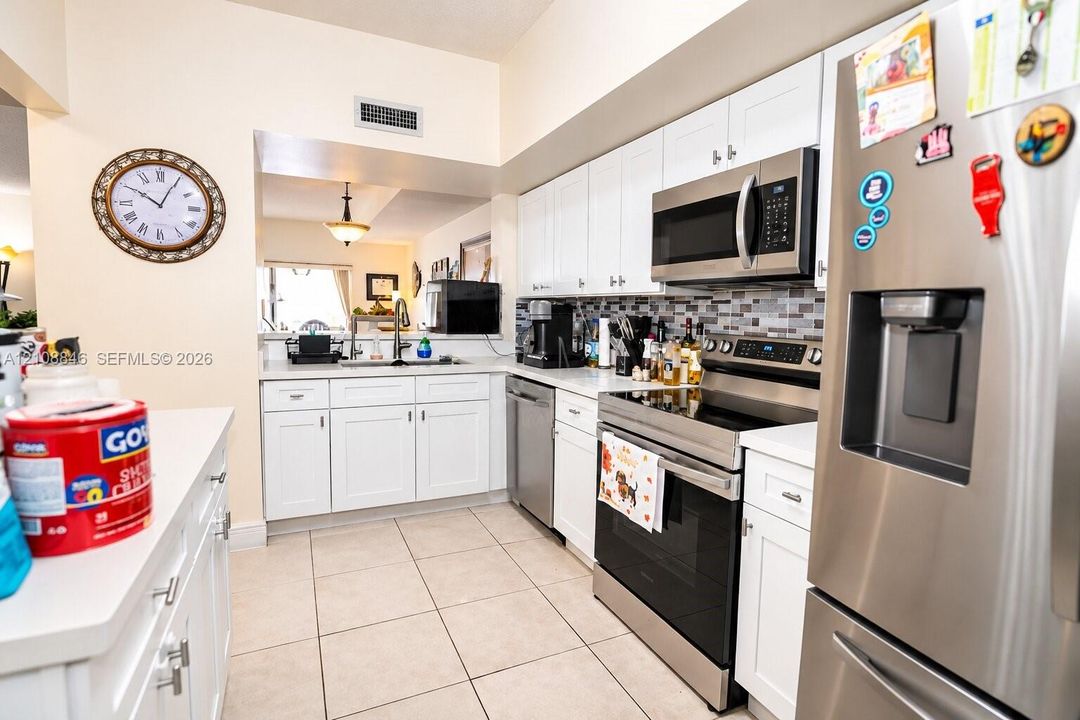 Kitchen featuring white cabinetry, stainless steel appliances, multi-toned tile backsplash, and light-toned tile flooring