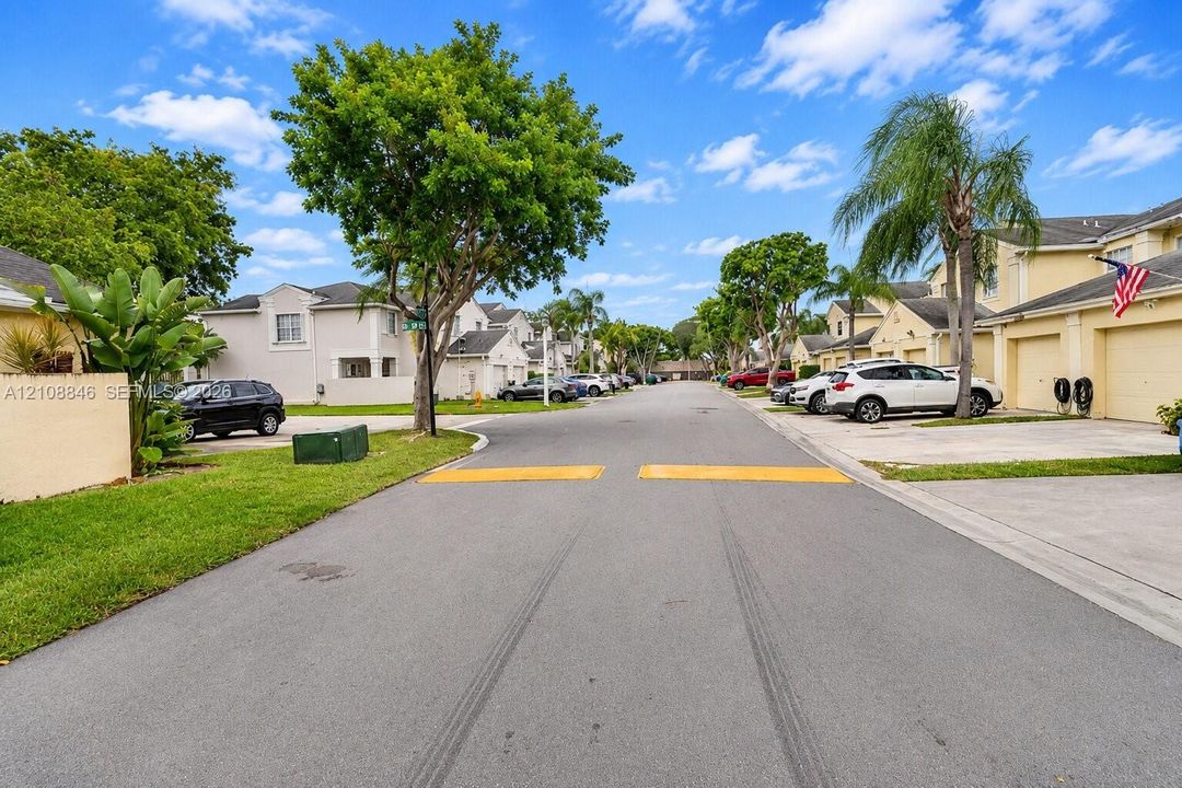 Multi-family residential community featuring stucco exterior finishes, concrete driveways, attached garages, paved streets, and mature landscaping