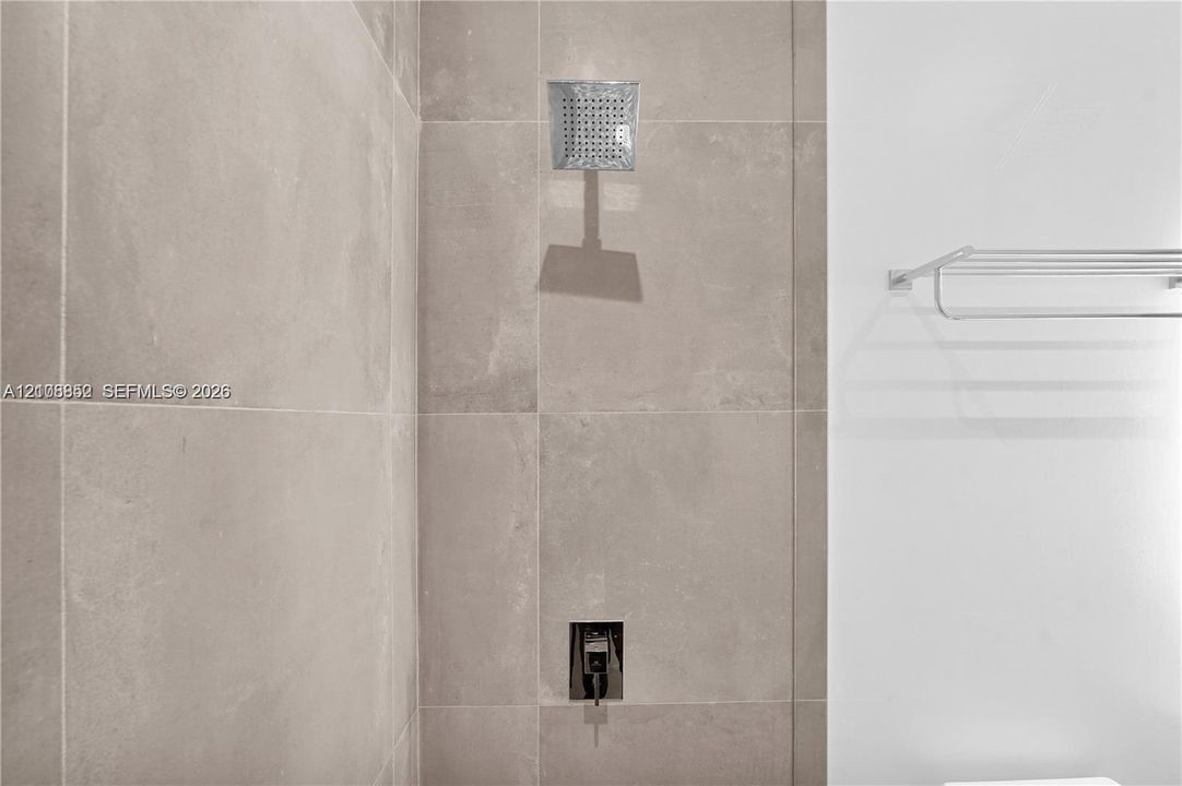 Shower featuring large-format neutral-toned wall tile, a square rainfall showerhead, a built-in single-handle shower valve, and a wall-mounted metal towel rack