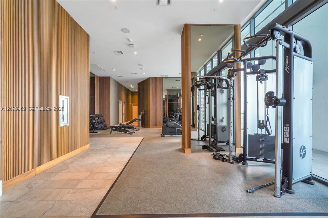 Fitness facility featuring vertical wood paneling, floor-to-ceiling windows, mirrored structural columns, and tiled flooring