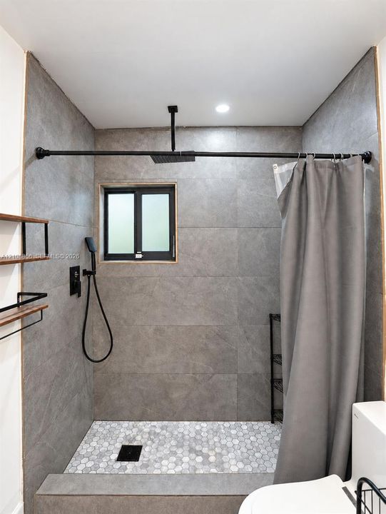 Walk-in shower featuring large-format grey tile surround, hexagonal floor tiling, a ceiling-mounted rainfall showerhead, and matte black plumbing fixtures