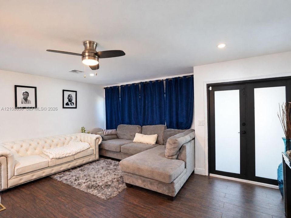 Wood-finish flooring, brushed metal ceiling fan with integrated lighting, and black-framed double doors with frosted glass panels