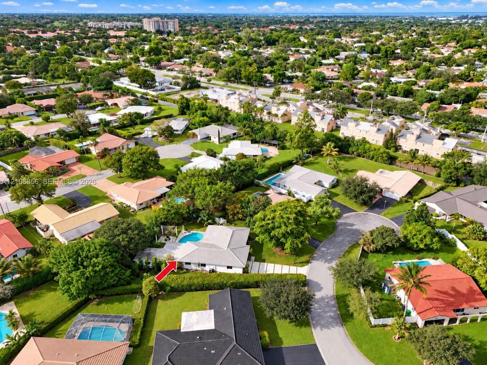 Aerial view of a residential property featuring an outdoor swimming pool, paved driveway, expansive lawn, and mature landscaping