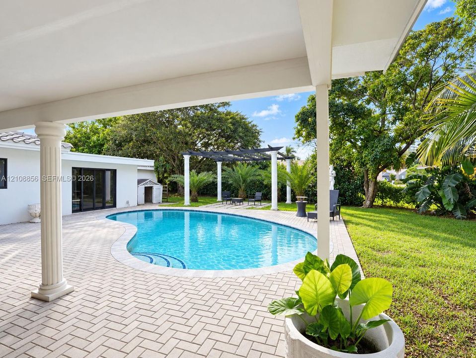 Covered patio with paver flooring, kidney-shaped pool, and custom pergola featuring white columns