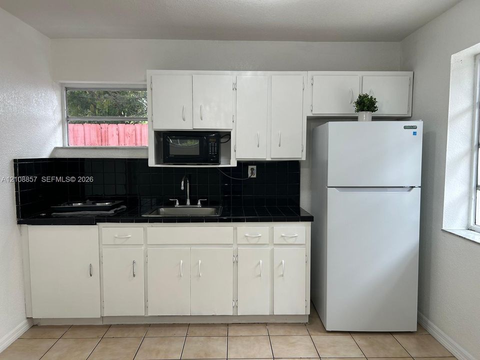 Kitchen featuring white cabinetry, contrasting black tile countertops and backsplash, integrated stainless steel sink, and ceramic tile flooring