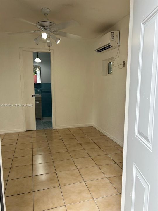 Interior space featuring tile flooring, a ceiling-mounted light fixture with a fan, a wall-mounted ductless air conditioning unit, and a sliding door