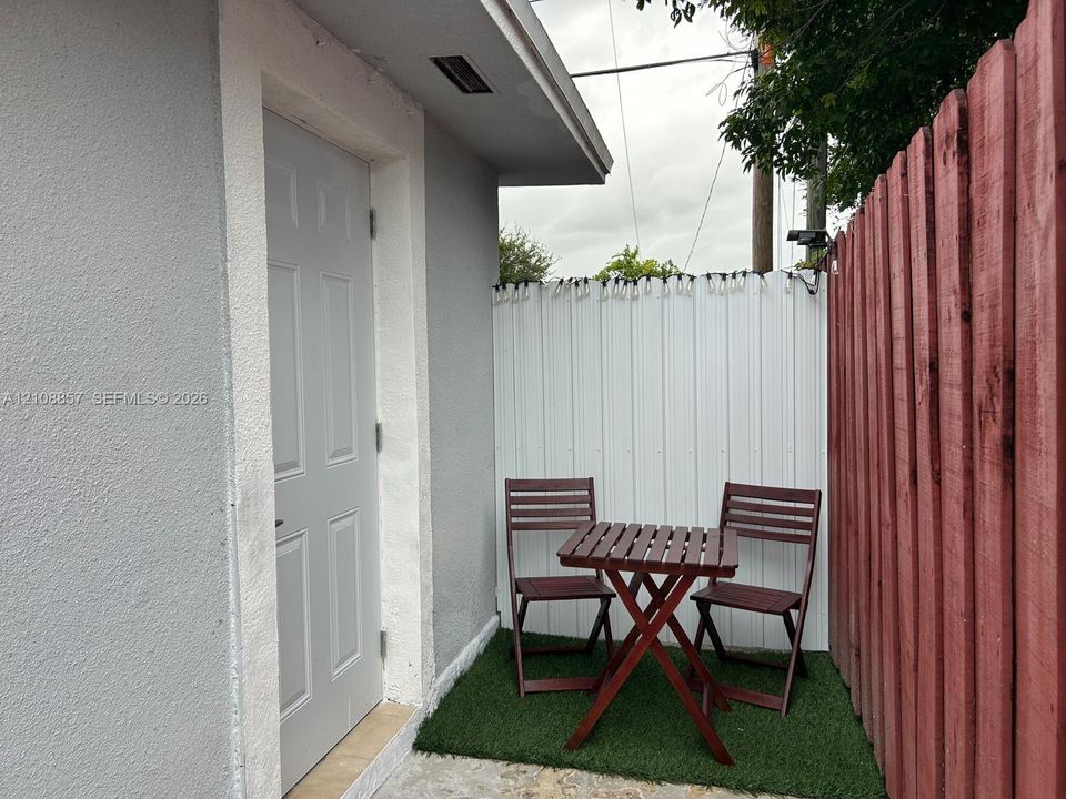 Exterior space featuring a light-toned stucco wall, a solid-panel door, and a private enclosed area with white metal fencing and red wood-slat perimeter fencing